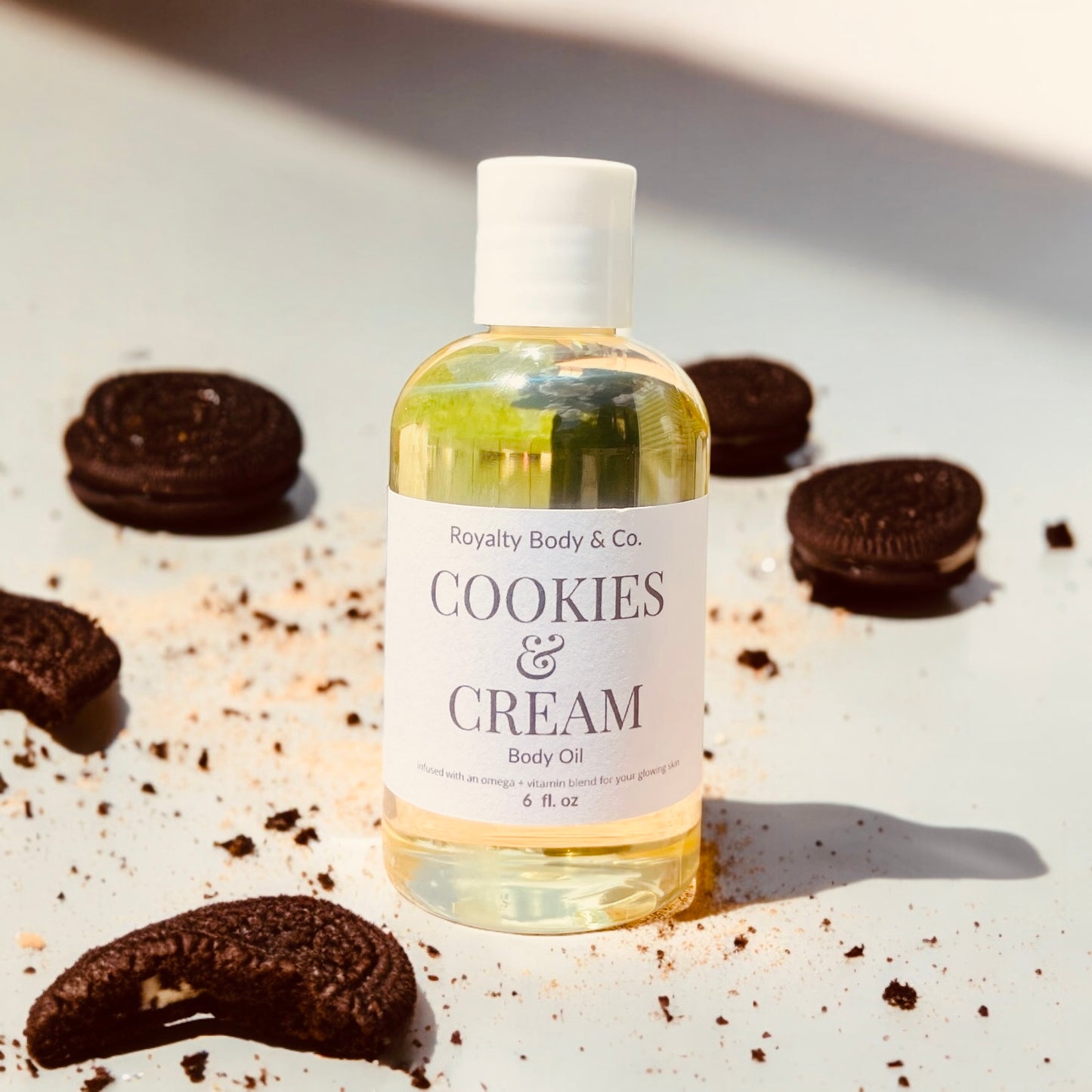 Royalty Body & Co.s hydrating Cookies & Cream Body Oil glistens among scattered Oreo cookies. Perfect for sensitive skin, the label shines, and cookie crumbs provide a playful touch.