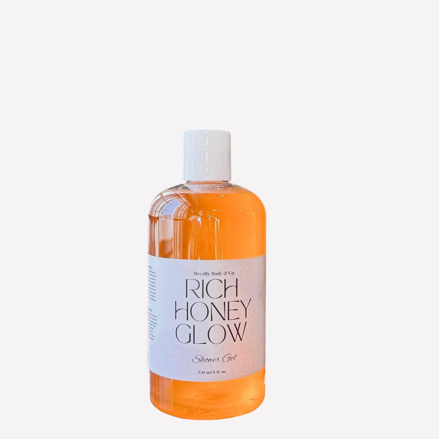 The Rich Honey Glow Shower Gel by Royalty Body Co. features a clear bottle with a white label showcasing its orange, hydrating formula. The label highlights Shower Gel and 236 ml/8 fl oz, while a sleek white screw cap completes this perfect self-care addition.